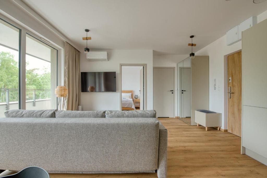 A modern hotel room with a large window, a sofa, a bedside table, and a wardrobe.