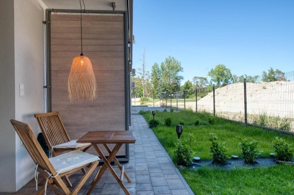 Een terras met een tafel en stoelen, een hangende lamp en uitzicht op een aangelegde tuin met een hek.