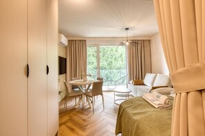 Habitación de hotel con cama, una mesa de comedor, sillas, un sofá y un balcón con cortinas.