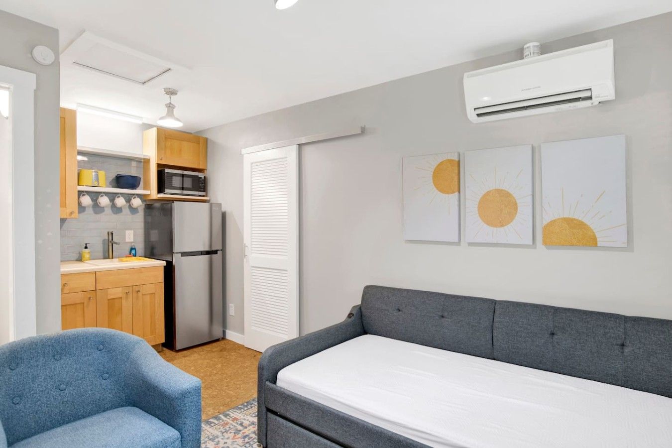 A compact living space with a kitchenette, a grey sofa, and a blue armchair.