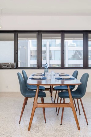 A dining area with a rectangular table set for four, surrounded by four chairs with wooden legs and dark upholstery. - Liiiving in Porto - Lobo Studio I (Porto)