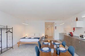 A modern, well-lit room with a bed, bedside table, and a dining area set for four. - Liiiving in Porto - Lobo Studio I (Porto)