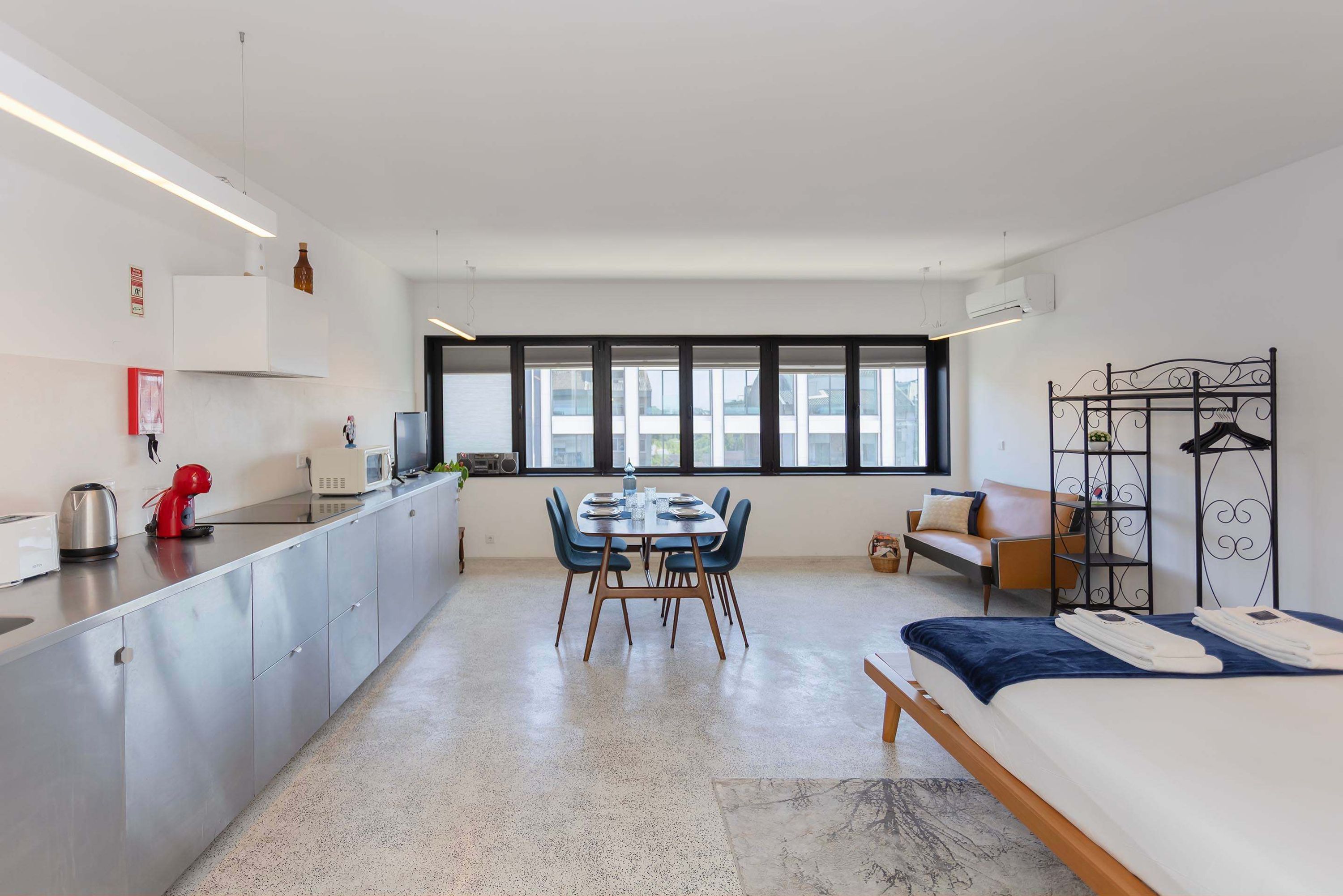 A modern, well-lit room with a kitchen area, dining table, and a bed.