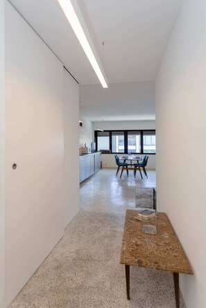 A modern office space with a long corridor, a meeting table with chairs, and a kitchenette area. - Liiiving in Porto - Lobo Studio I (Porto)