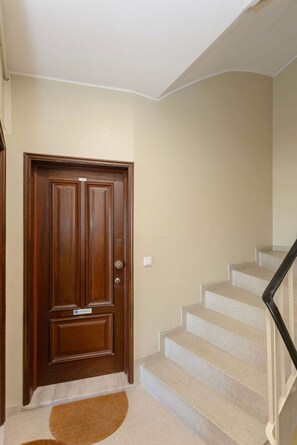 A wooden door with a sign indicating 'ENTRADA' (entrance), a carpeted staircase with a handrail, and a plain wall with a light texture. - Liiiving in Porto - Lobo Studio I (Porto)