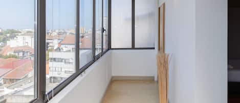 A balcony with a view of buildings, a chair, and a table with plates.