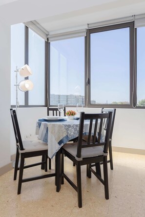 A dining area with a table set for two, two chairs, a lamp, and a view of the city through large windows. - Liiiving in Porto - Lobo Studio II (Porto)