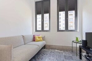 A living room with a sofa, a small table with a plant and a pair of shoes, and a television. - Liiiving in Porto - Design Loft Marqu s (Porto)