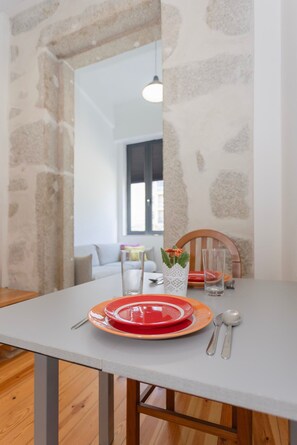 A dining table with red and orange plates, silverware, and a glass. A white table runner and a potted plant are on the table. The room has a stone wall and a wooden floor. - Liiiving in Porto - Design Loft Marqu s (Porto)