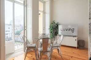 A modern living room with a glass dining table, clear chairs, a potted plant, and a TV screen displaying 'LIVING IS EASY'. - Downtown Balcony Studio II (Porto)