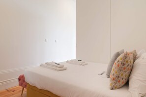 A neatly made bed with folded towels, a single pillow, and a bedside table with a book. - Downtown Balcony Studio II (Porto)