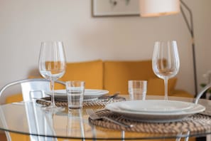 Taula de menjador amb vidrieres i plats nets, un calaix d'estil trenat i un sofà groc al fons.