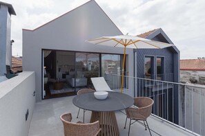 Ein moderner Balkon mit Sitzgelegenheit, Tisch und einem großen Sonnenschirm.