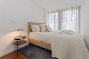 Ein Hotelzimmer mit einem Bett, einem Nachttisch mit Lampe, einem Fenster mit Vorhängen und einem auf dem Bett gefalteten Handtuch.