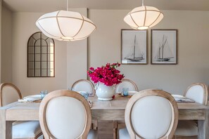 Un coin repas avec une table en bois, des chaises blanches, un vase rempli de fleurs roses et deux tableaux encadrés accrochés au mur.