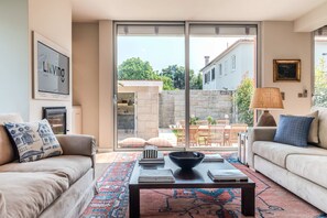 A living room with a sofa, a coffee table, and a view of a courtyard with outdoor furniture. - Liiiving in Porto - Foz Garden House 3 bdr (Porto)
