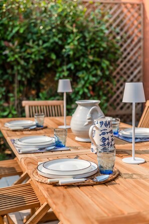 Une table de salle à manger en bois, mise avec des assiettes, des verres et un pichet, entourée de chaises et de lampes.