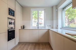A modern kitchen with built-in appliances, a window with a view, and a wooden floor. - Liiiving in Porto - Foz Garden House 3 bdr (Porto)