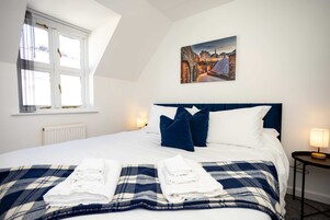 A hotel room with a bed, a painting, a window, and a radiator.
