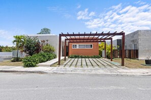 Un edificio moderno con un porche con pérgola, una ventana pequeña y un sendero de hormigón que lleva a la puerta.