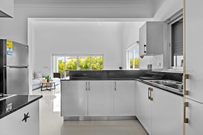 A modern kitchen with white cabinets, a black countertop, and a stainless steel refrigerator.