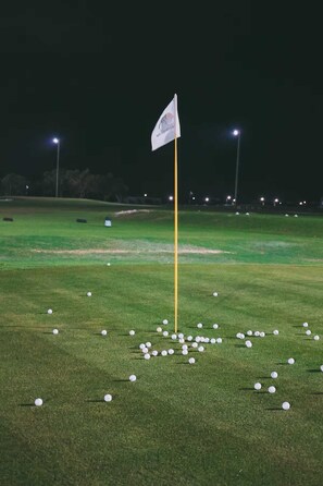 Un campo de golf de noche con un mástil de bandera en el centro rodeado de pelotas de golf dispersas.