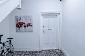 A hallway with a white door labeled 'Eastgate Hideaway,' a painting of a rainy street scene, and a bicycle. - Hideaway City Centre Flat in Chester Sleeps 2 (Chester)