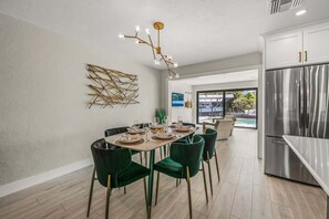 Eine moderne Küche mit einem Edelstahl-Kühlschrank, einem Essbereich mit rundem Tisch und grünen Stühlen sowie einem dekorativen Wandbild.