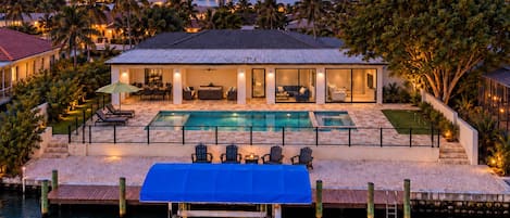 A waterfront property with a swimming pool, outdoor seating, and a dock extending into the water.