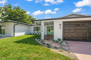 Ein Bungalow mit Garage, überdachter Veranda und gepflegtem Rasen.