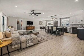 Una sala de estar moderna con sofá, mesa de centro y televisor. Cuenta con una zona de cocina, mesa y sillas.