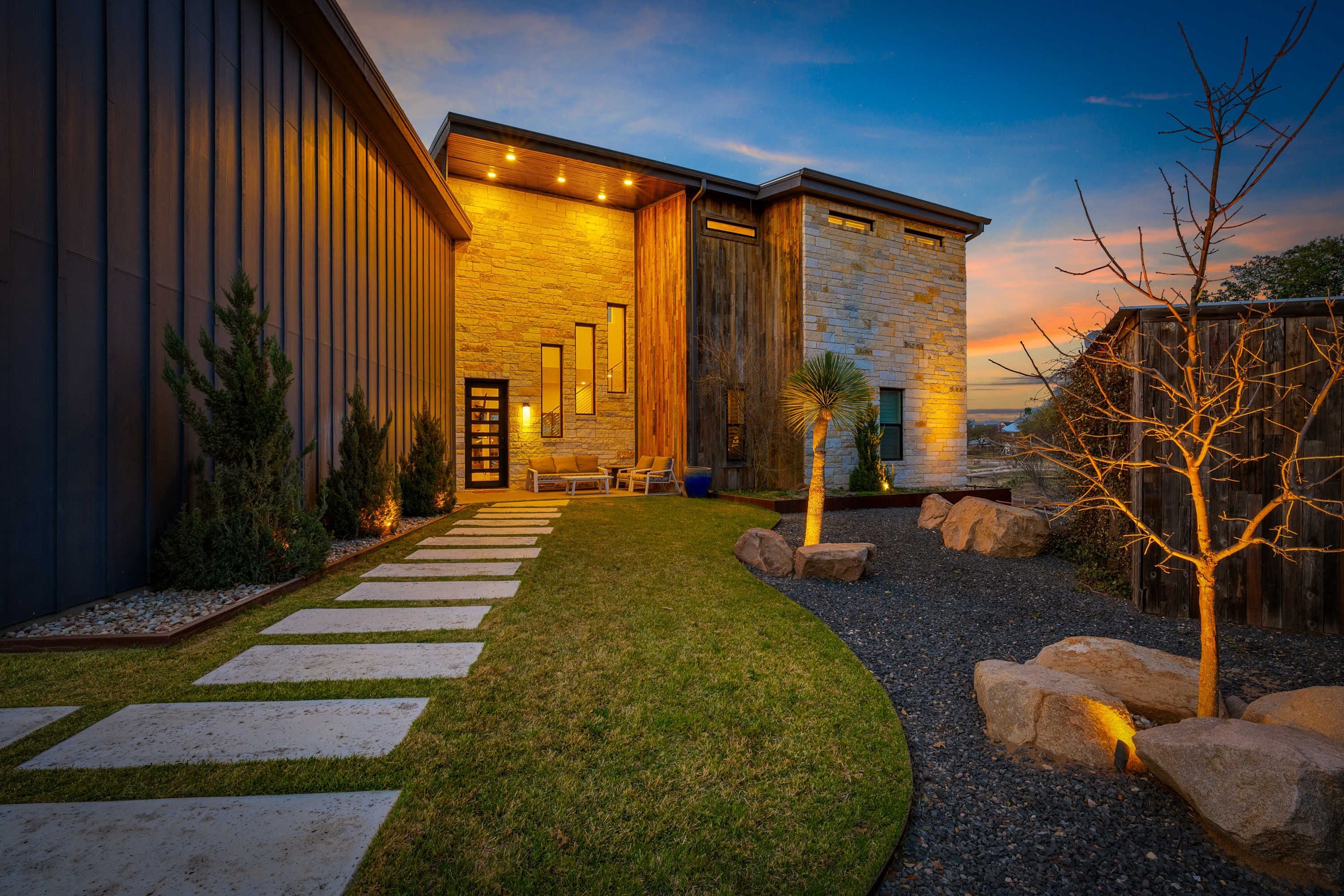 A modern house with a stone facade, a wooden deck, and a well-maintained lawn.