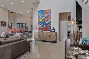 A spacious living room with a large abstract painting, a modern sofa, and a dining area with a unique cabinet. - Lake Buchanan Bliss Pool Spa Lakefront Beach (Burnet)