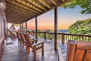 A wooden deck with chairs and a table, overlooking a scenic landscape with trees and hills.