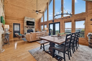 A spacious room with a fireplace, a dining table with chairs, and large windows offering a view. - Ski-out to Hatley Pointe Hot Tub Sleeps 8 (Mars Hill)