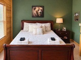 A neatly made bed with a headboard, a bedside lamp, and a wall-mounted picture of a bear.