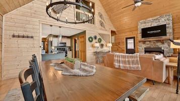 A spacious living area with a wooden dining table, a fireplace, and a television mounted on a stone wall.