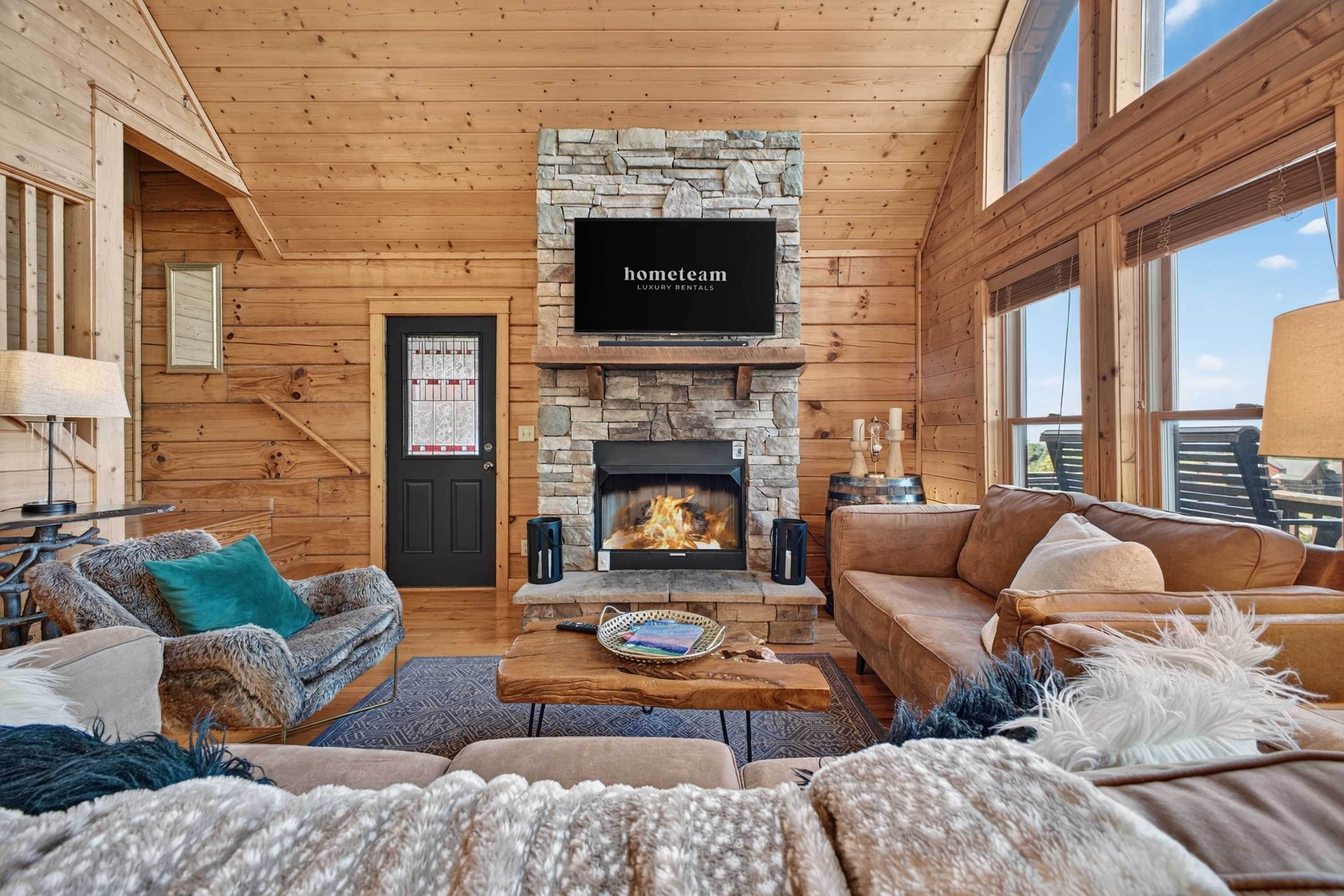 A cozy living room with a stone fireplace, wooden walls, and a television mounted above it.