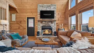 A cozy living room with a stone fireplace, wooden walls, and a television mounted above it.