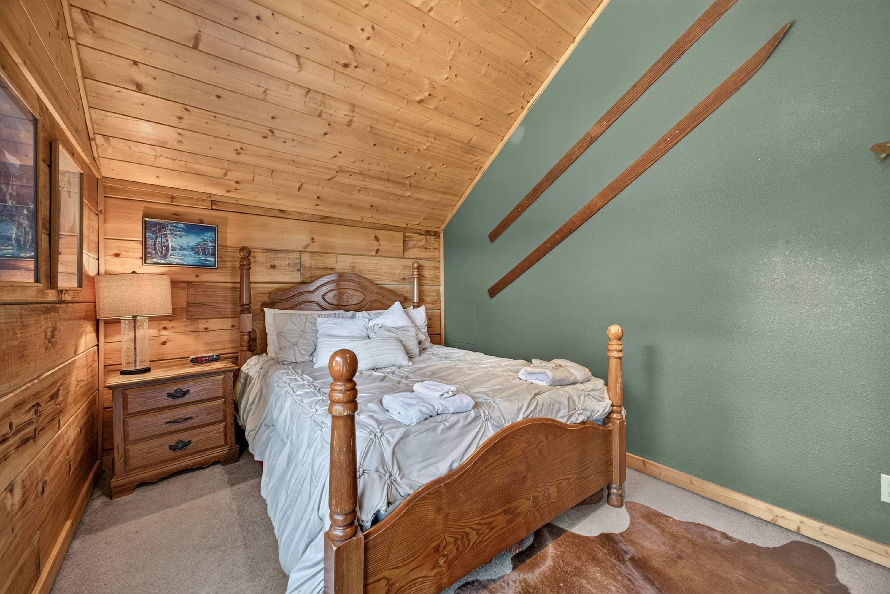A wooden bedroom with a bed, nightstands, a lamp, and a painting on the wall.