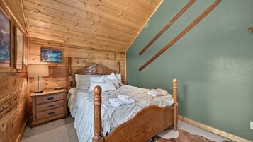 A wooden bedroom with a bed, nightstands, a lamp, and a painting on the wall.