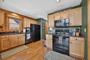 A kitchen with wooden cabinets, a black refrigerator, a stove, and a microwave. - Ski-out to Hatley Pointe Hot Tub Sleeps 8 (Mars Hill)