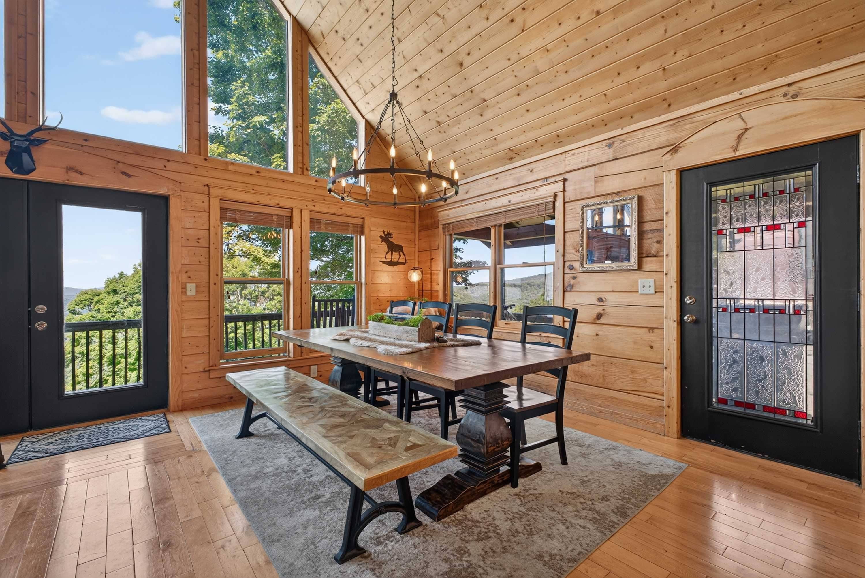 A wooden cabin interior with a dining table, benches, and a chandelier.