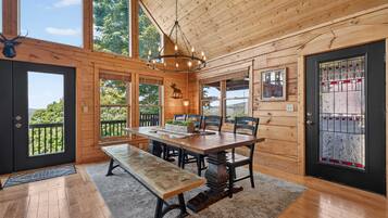 A wooden cabin interior with a dining table, benches, and a chandelier.