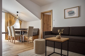 A modern living room with a wooden dining table, chairs, a sofa, and a small side table with vases. - Penthouse Suite With Outdoor Sauna (Gaschurn)