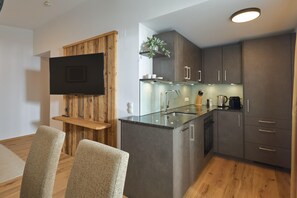 A modern kitchen with a flat-screen TV mounted on a wooden panel, a glass island counter, and stainless steel appliances. - Penthouse Suite With Outdoor Sauna (Gaschurn)