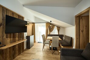 Een moderne leefruimte met een flatscreen televisie aan een houten wand, een eethoek met tafel en stoelen, en een gezellige zithoek met een bank en fauteuils.
