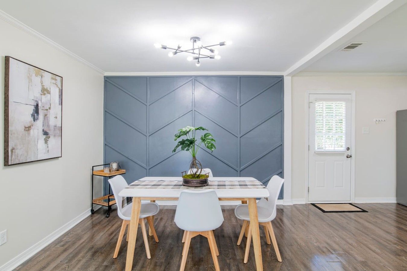 A dining area with a table, chairs, a plant centerpiece, and a geometric wall design.