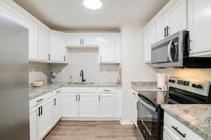 A modern kitchen with white cabinetry, a granite countertop, a stainless steel refrigerator, a microwave, and a built-in oven. - South Alabama Home near Colleges (Mobile)