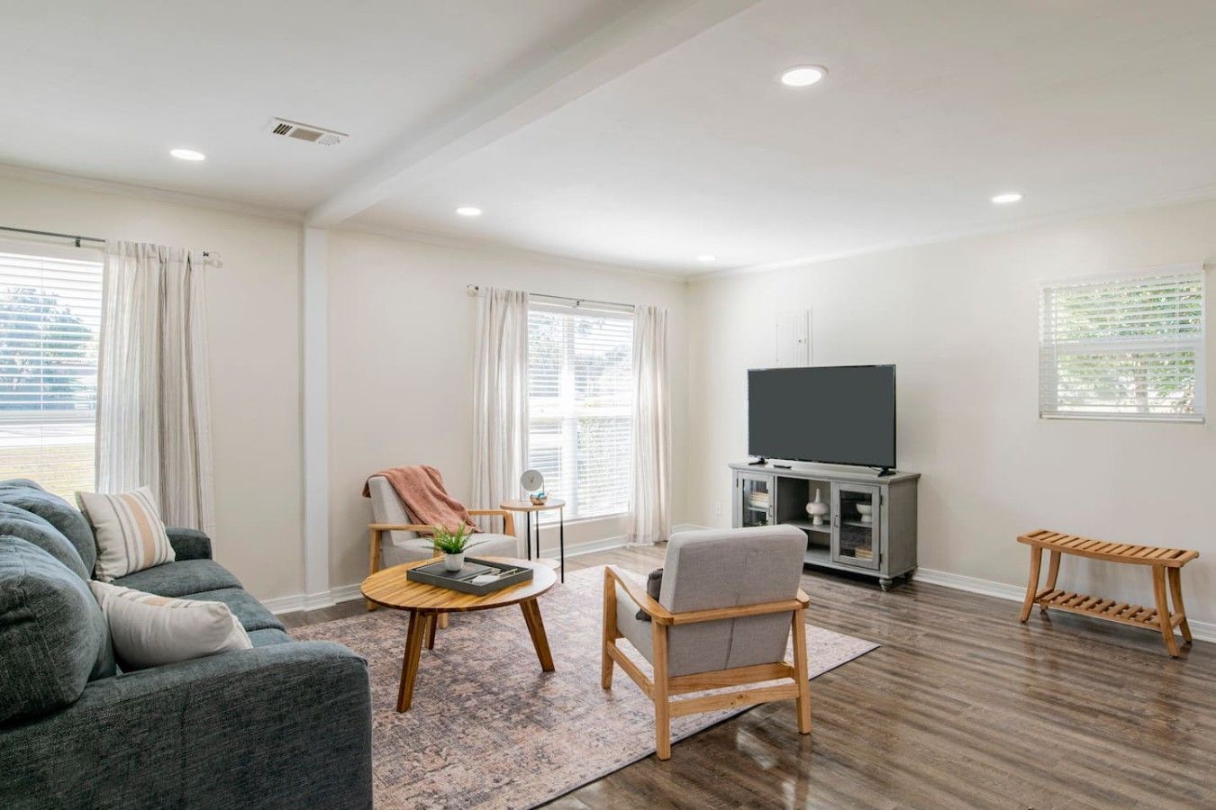 Una sala moderna con un sofá, un sillón, una mesa de centro y un televisor sobre un mueble.